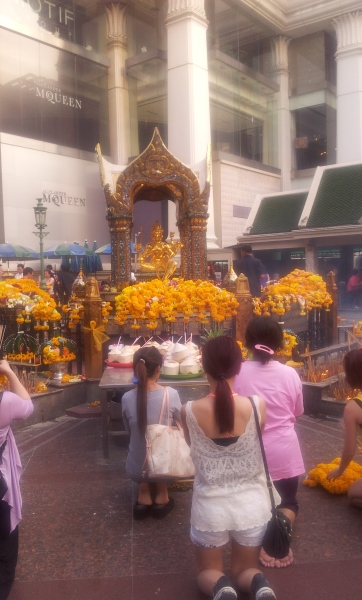 The different faces of Bangkok: designer shop Alexander McQueen stands behind worshippers at the Erawan shrine in central Bangkok 